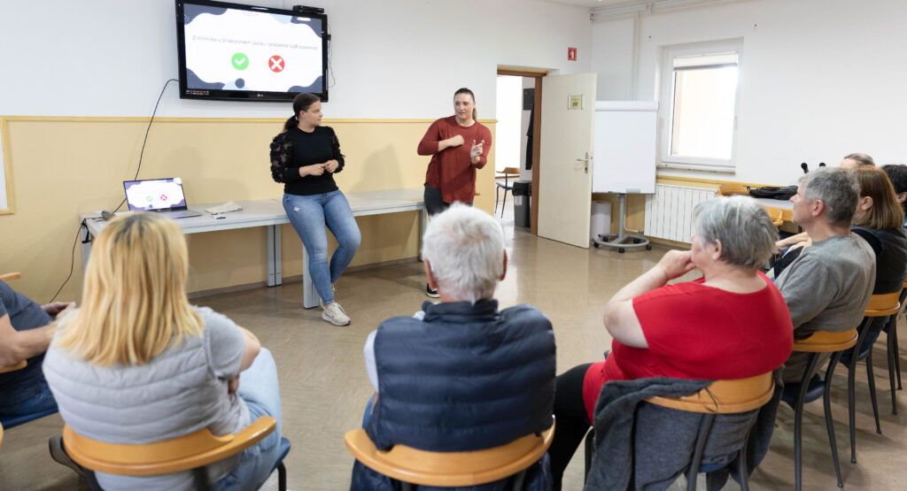 Poslušalci spremljajo predavanje. Daša kreta. Jerneja posluša. 