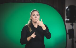 Daša Peperko tolmači v mednarodne kretnje, ozadje je zeleno.